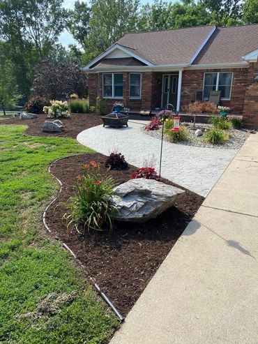Front yard with brick house, curved gravel path, flower beds, and large decorative rocks by a sidewalk