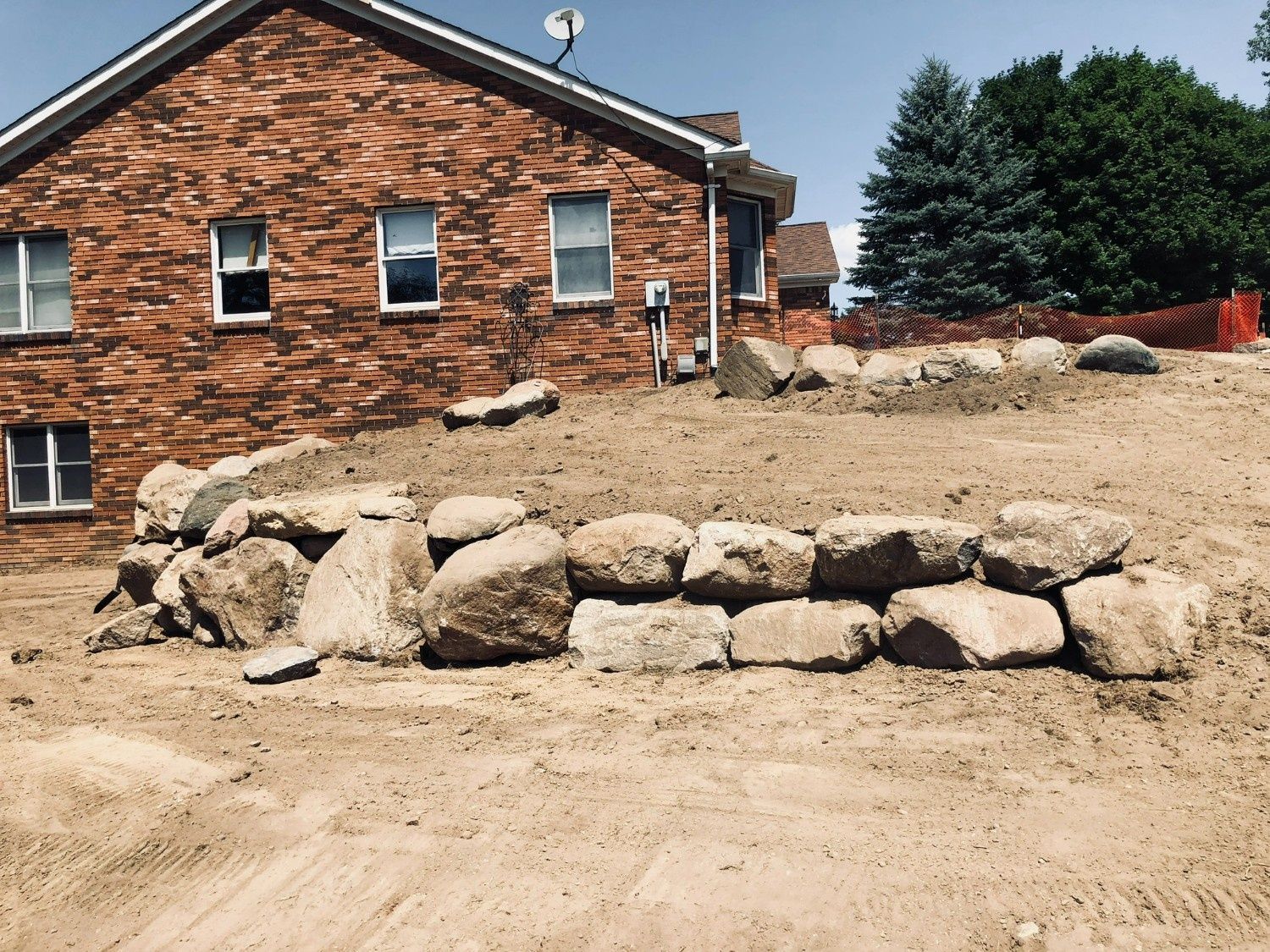 Rock retaining wall in front of a brick house on a dirt slope