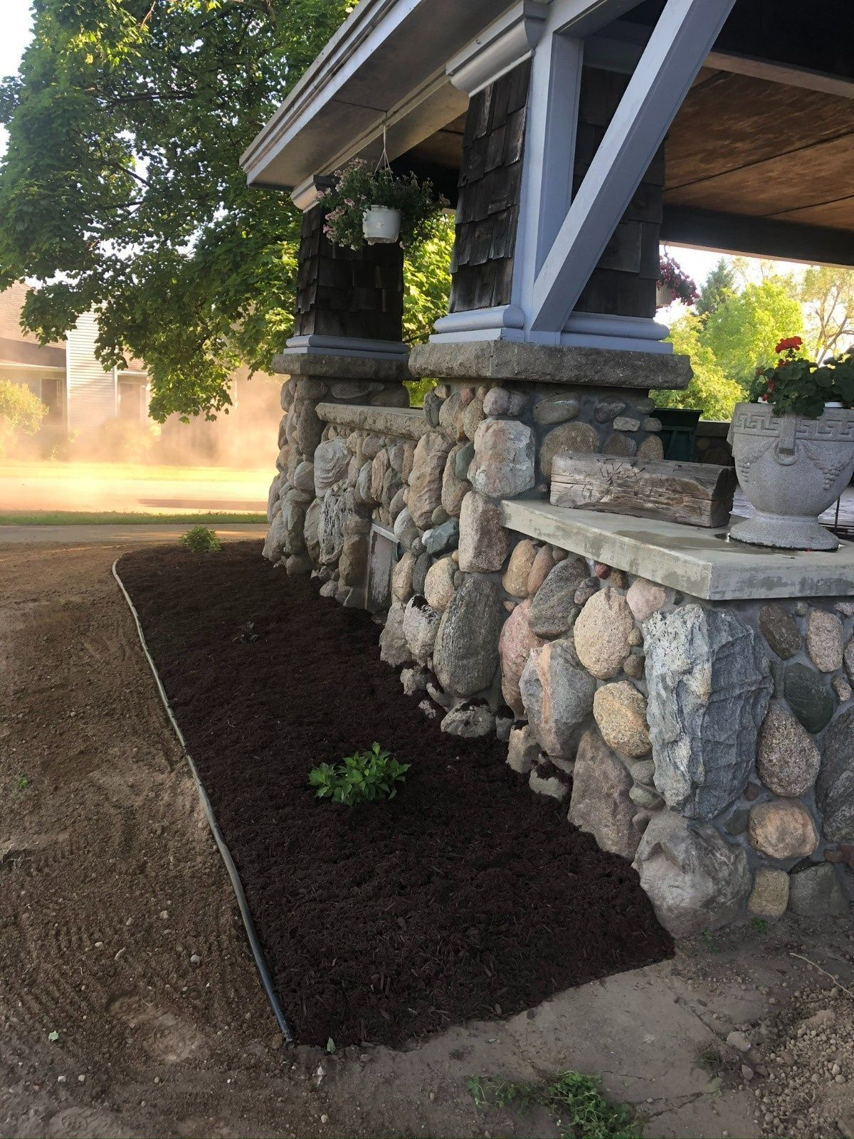 Stone retaining wall with fresh dark mulch and a small plant beneath a covered porch