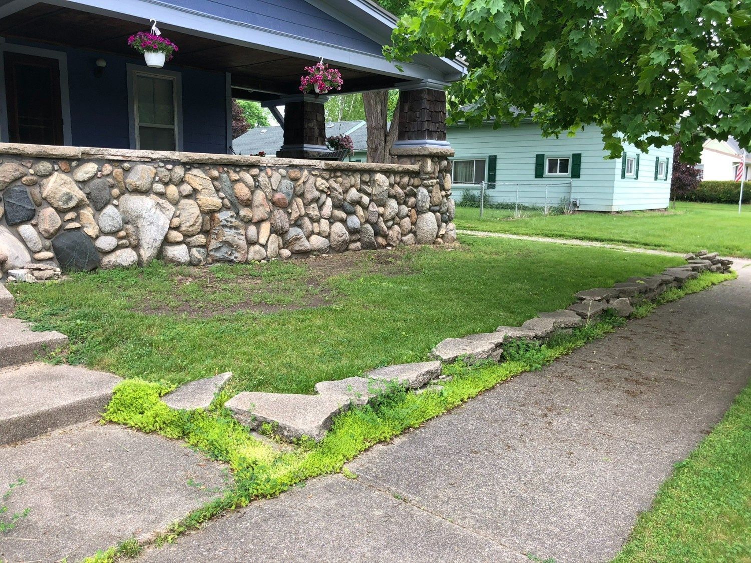 Stone house with flower baskets, grassy yard, and concrete walkway beside a driveway