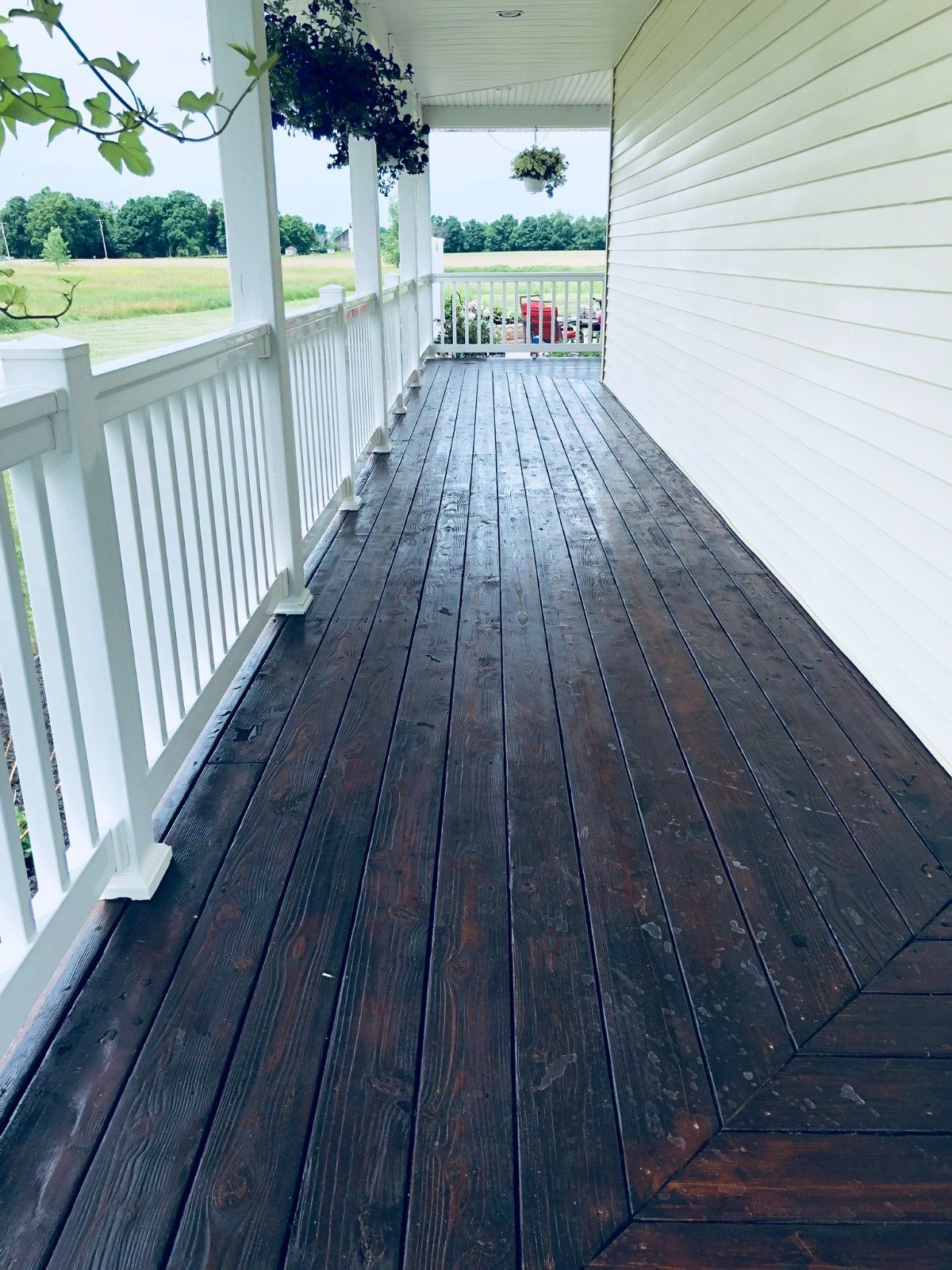 Covered porch with white railing and dark wooden floor overlooking a green yard