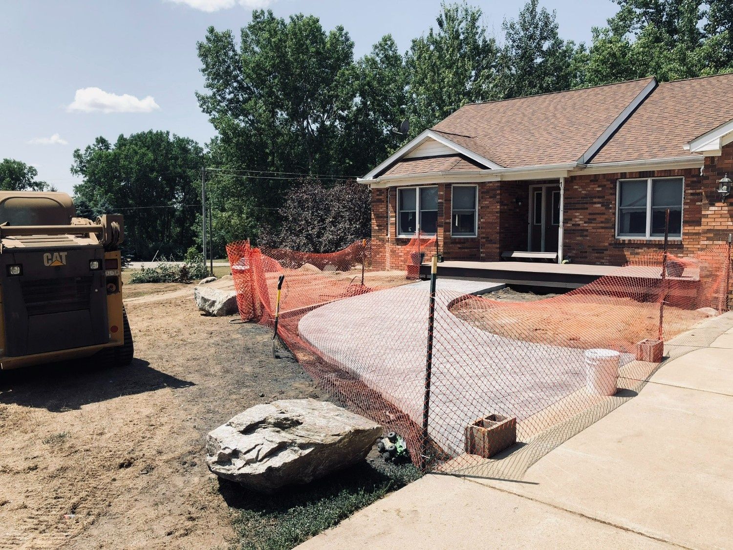 Construction site beside a brick house with orange safety fencing, gravel, and a parked truck