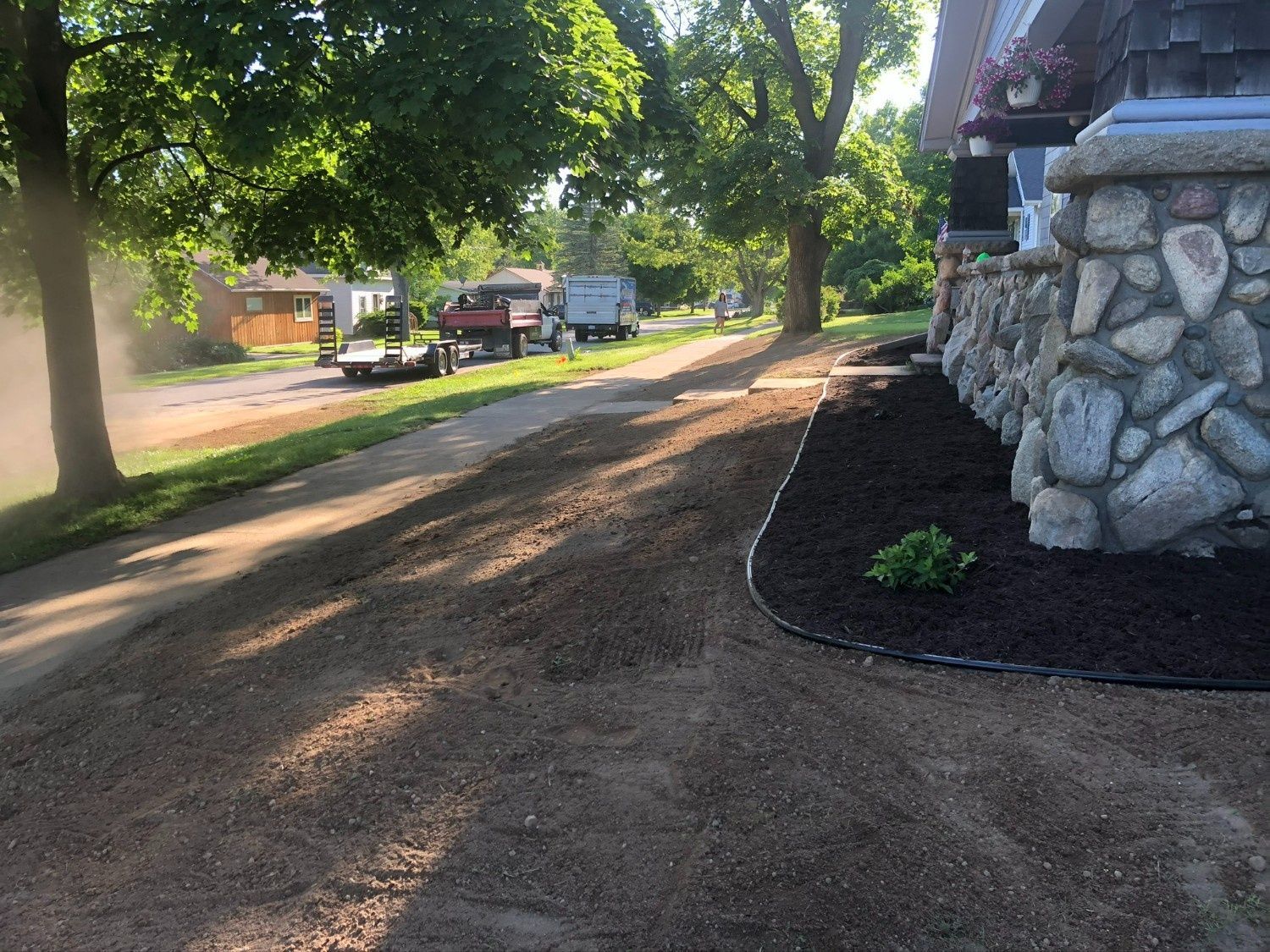 Gravel driveway beside a stone building, with trees and parked trucks in the background.