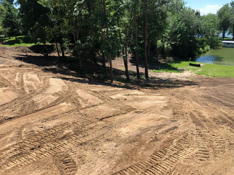 Freshly graded dirt clearing beside trees and a pond on a sunny day