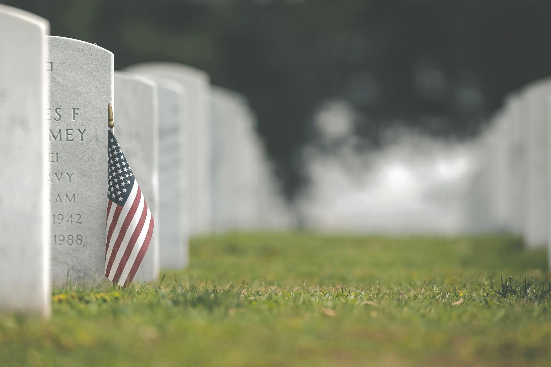 Rows of white gravestones in a cemetery, one with a small American flag