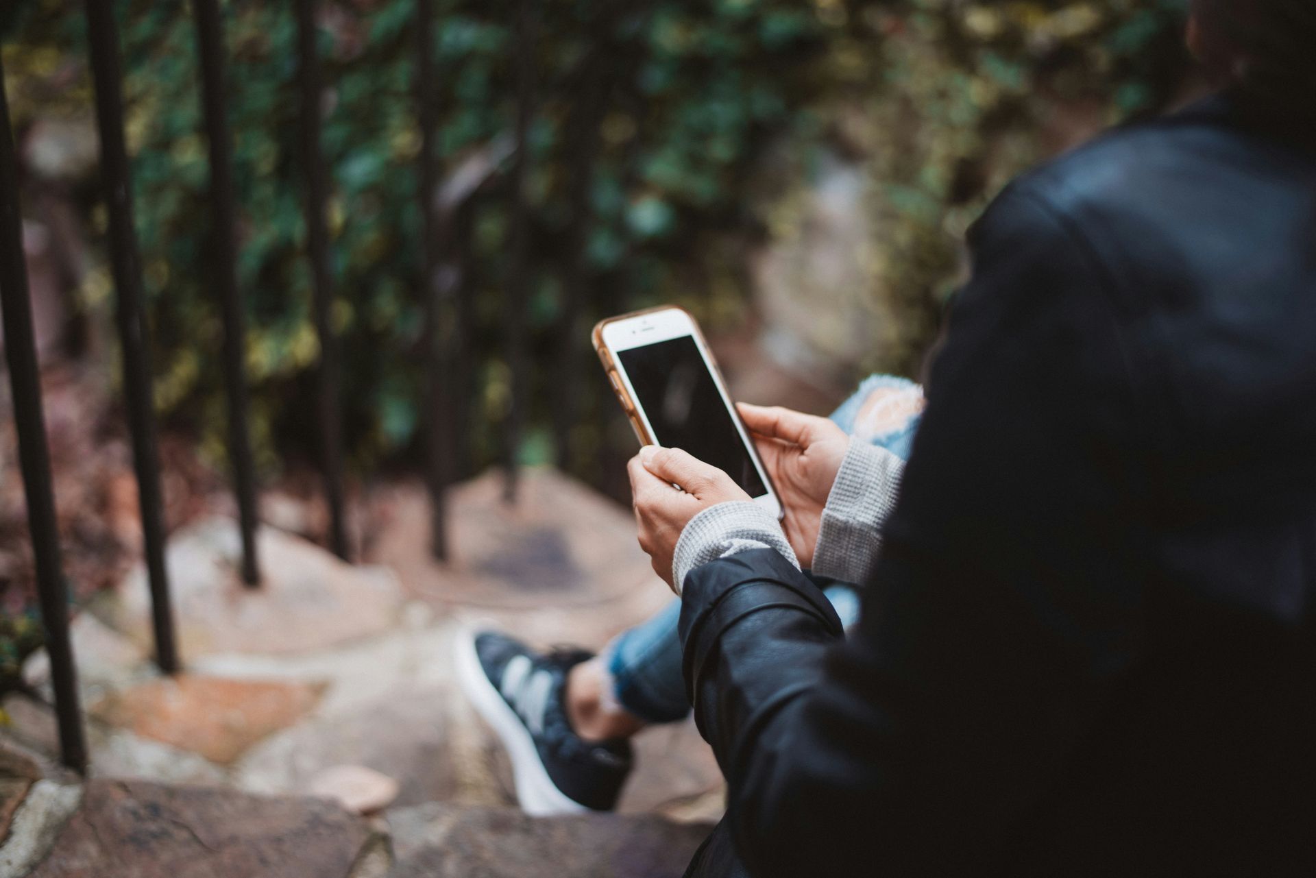 Person holding a smartphone outdoors on a wooded path with blurred trees in the background