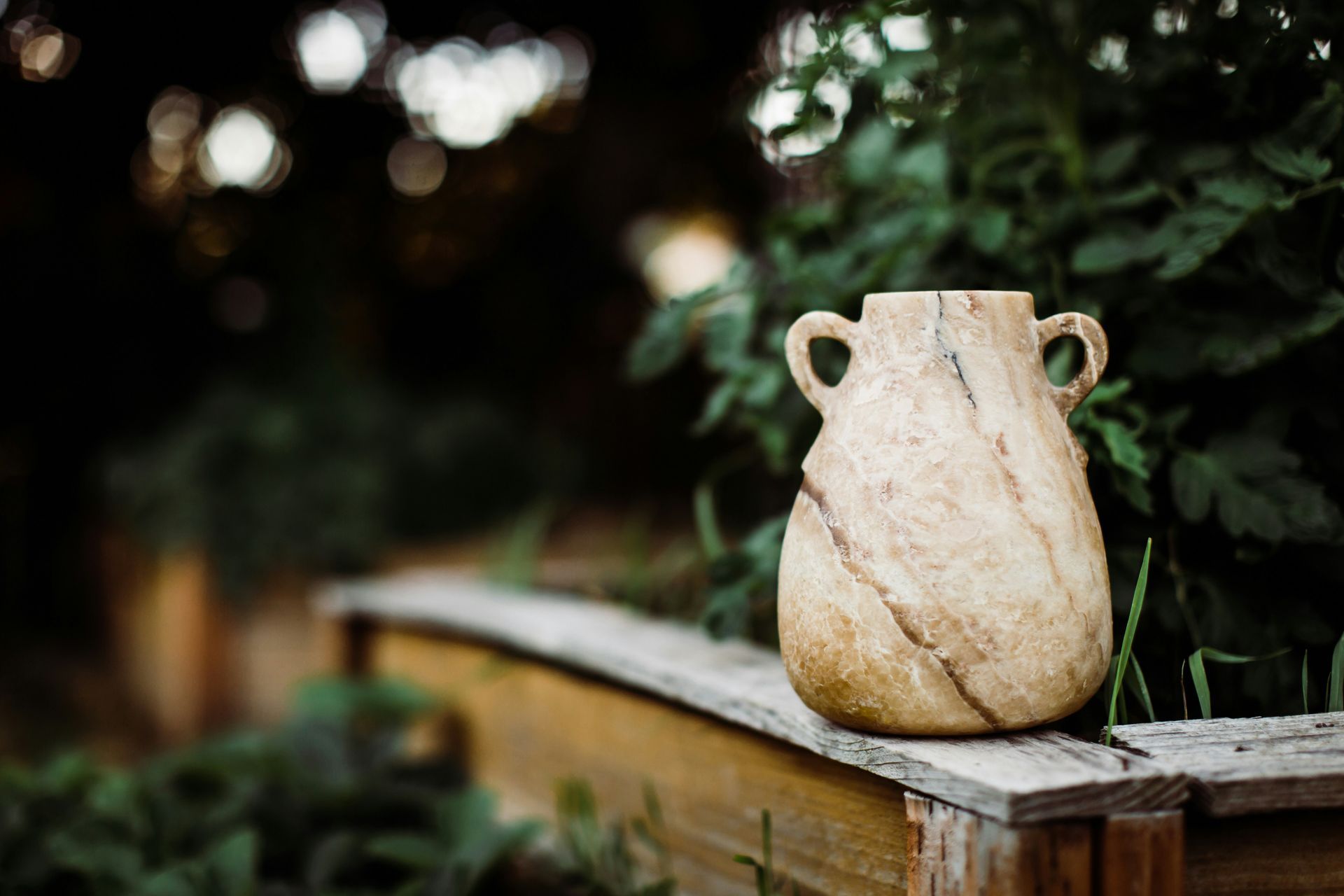 Weathered stone vase on a wooden railing with blurred greenery in the background