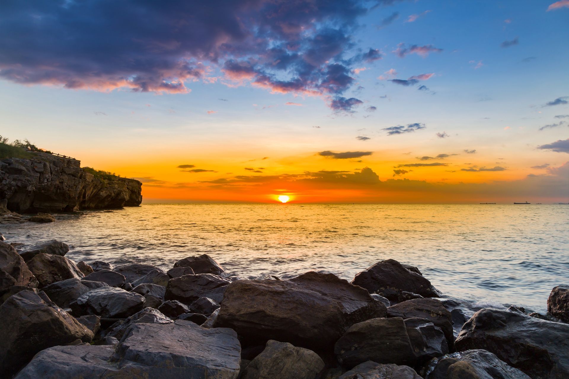 Sunset over rocky shoreline with orange sky and calm ocean waves