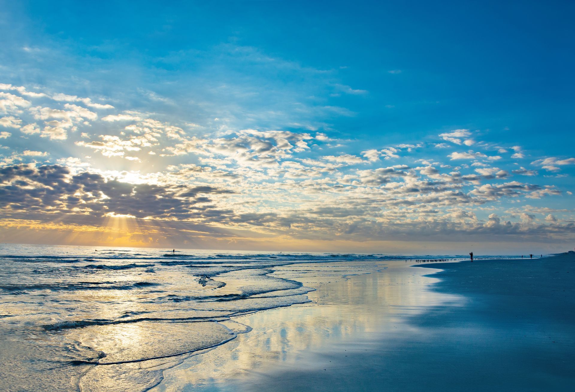 Sunrise over a calm beach with gentle waves and a reflective wet shoreline