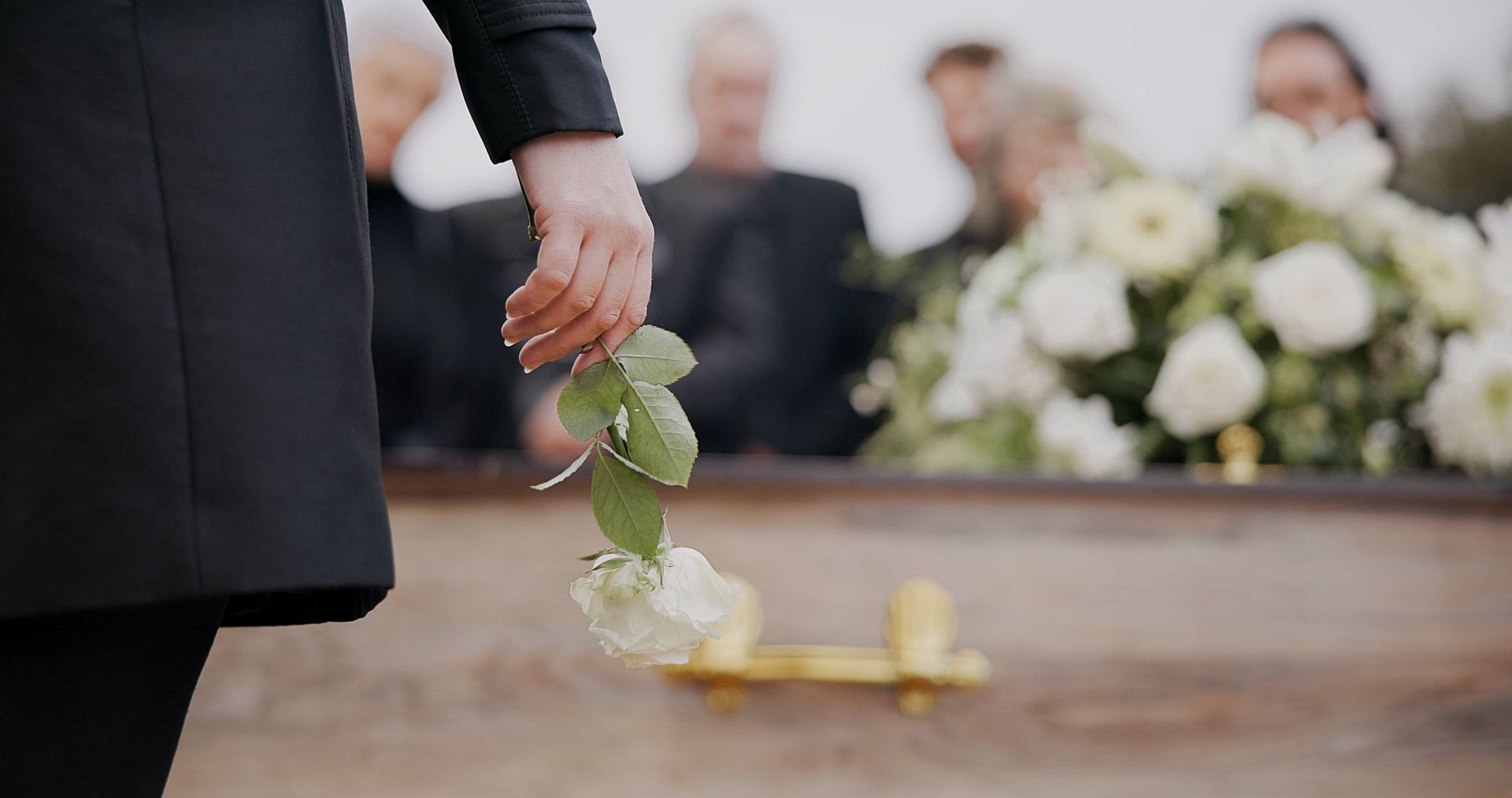 Person holding white flowers over a coffin at a funeral service