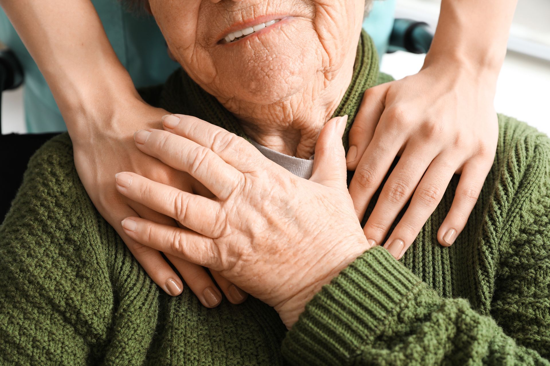 Hands gently resting on an elderly person in a green sweater