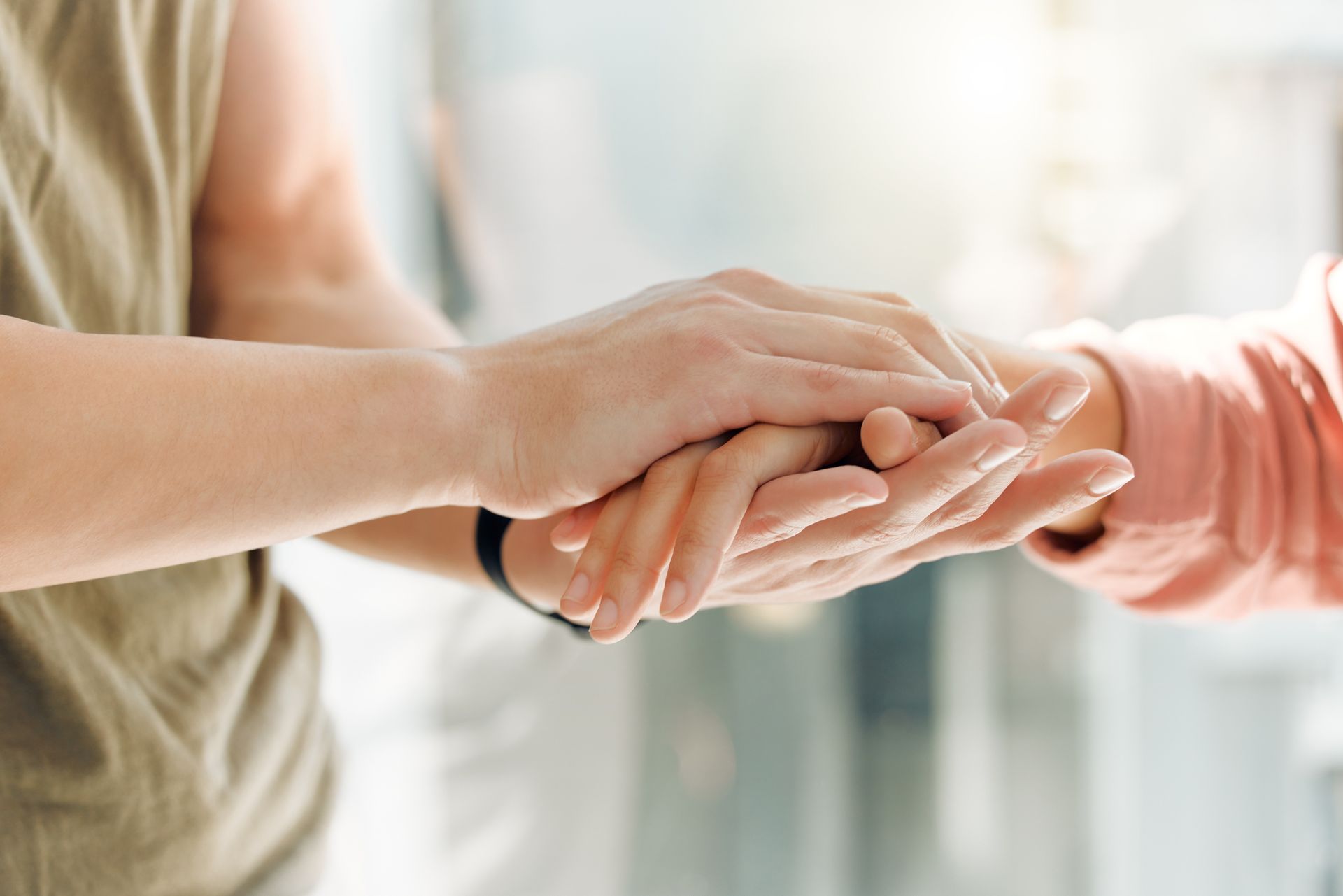 Two hands gently holding in a bright, softly blurred indoor setting