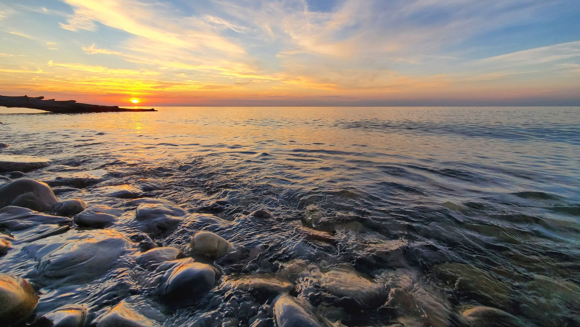 Sunset over a rocky shoreline with gentle waves and golden light reflecting on the water