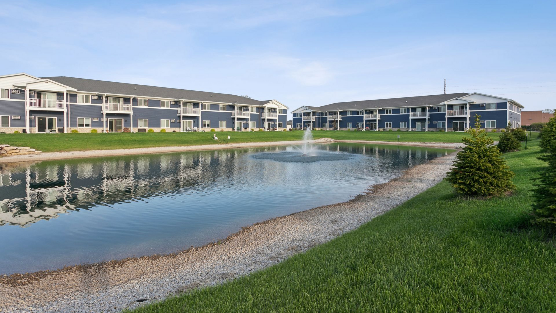 Apartment building with beige siding, wooden balconies, and a landscaped lawn under a blue sky