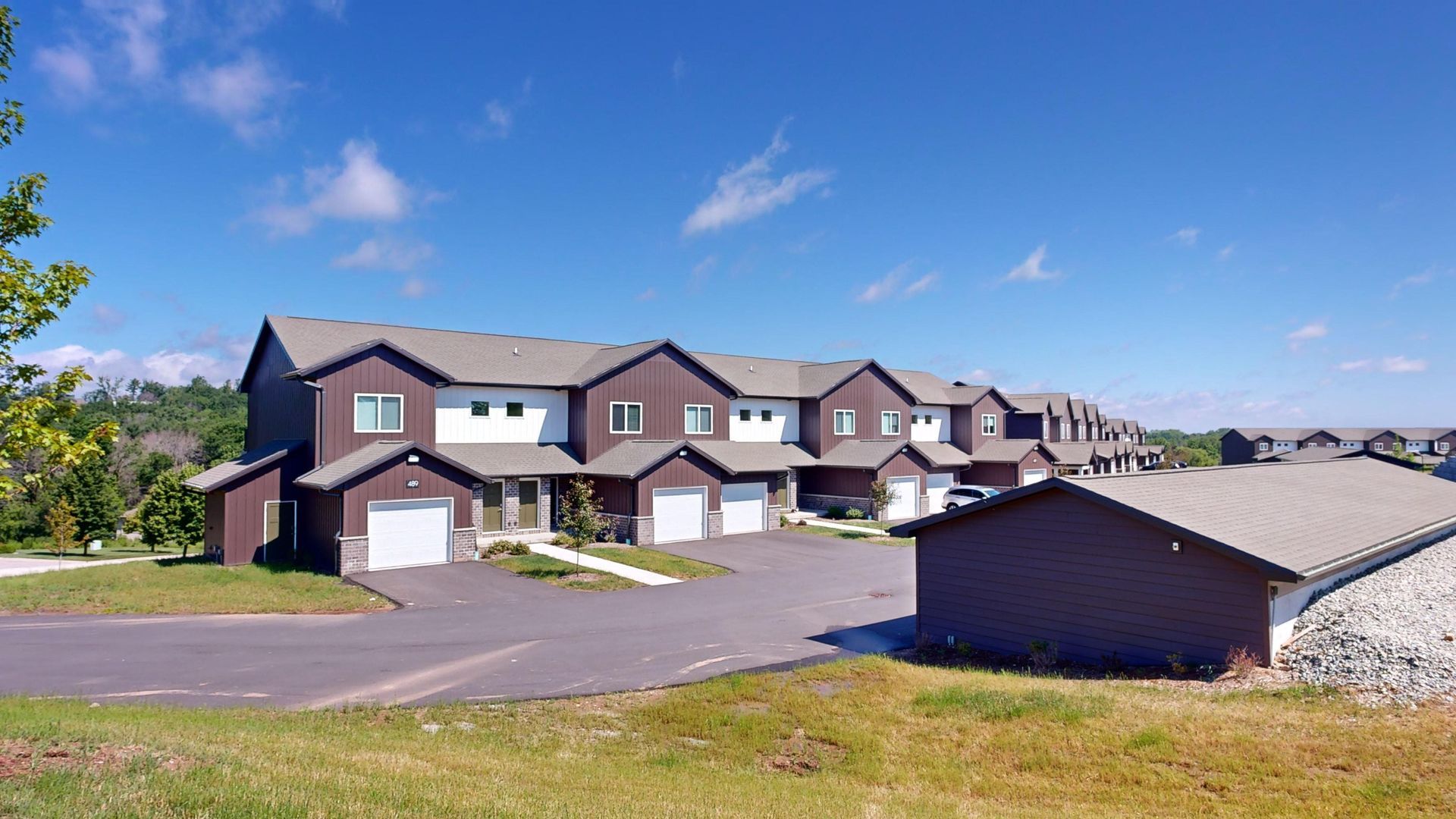Row of brown townhouses along a suburban street under a bright blue sky