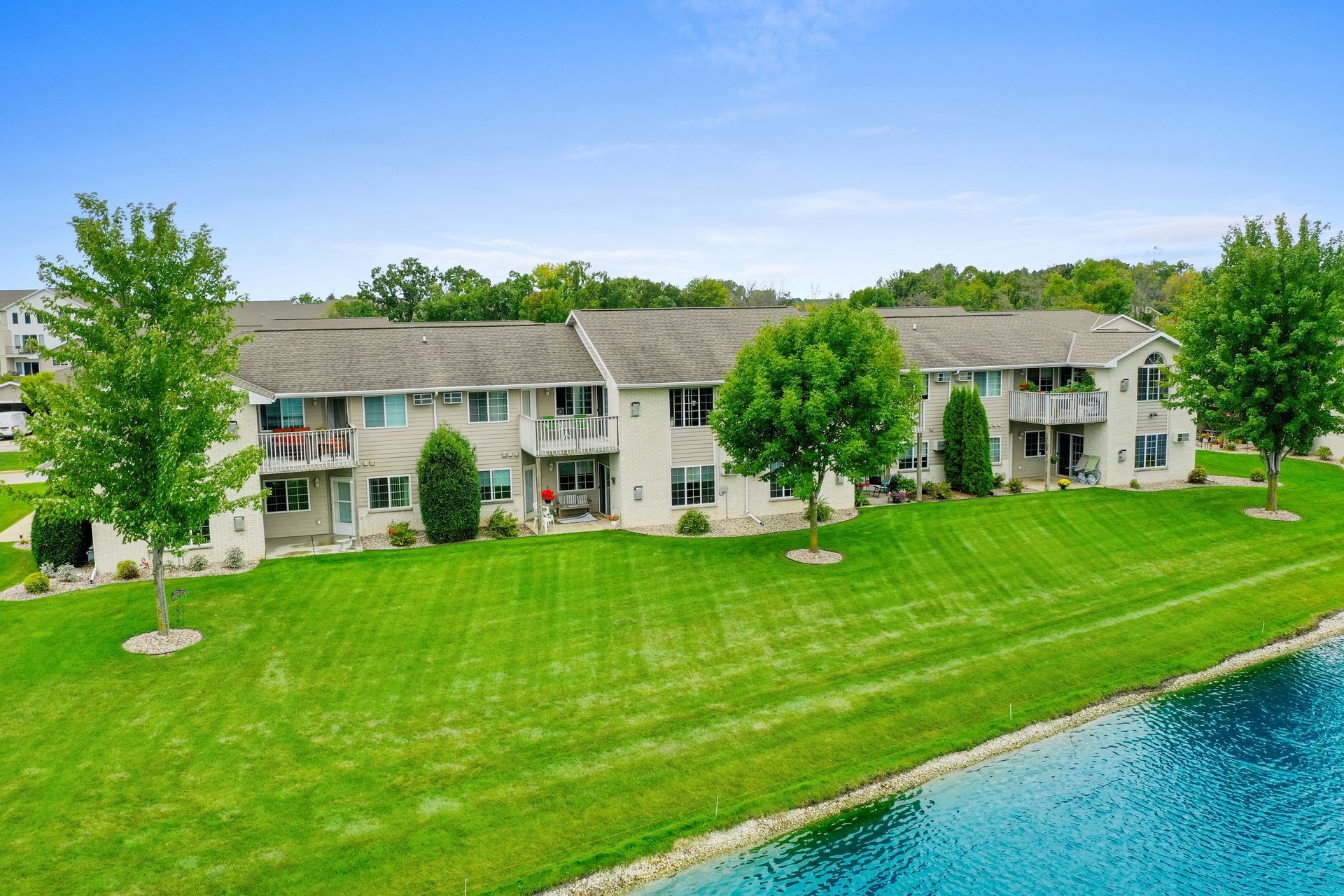 Lakeside apartment building with a green lawn and trees beside blue water