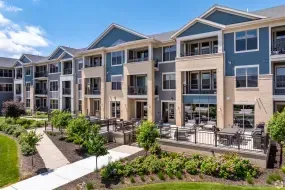 Modern apartment complex with balconies, patio seating, and landscaped walkways under a blue sky