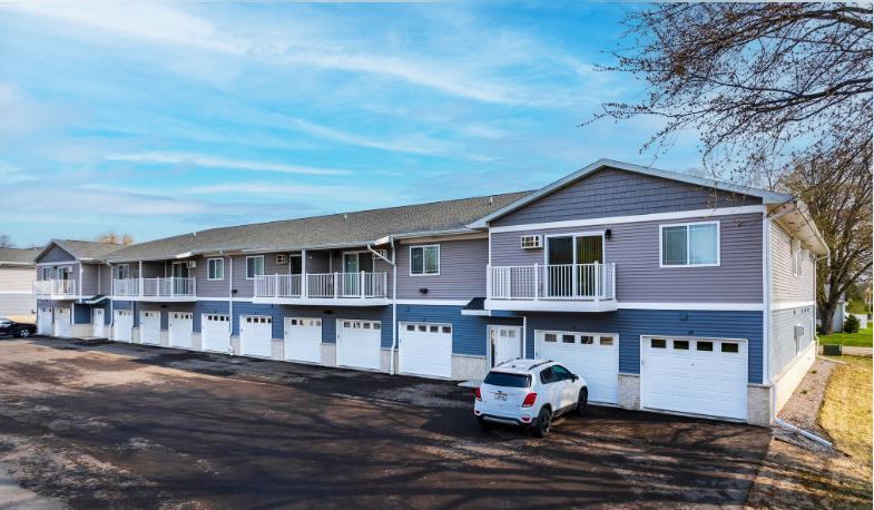Row of gray townhouses with garages and a white SUV parked outside under a blue sky