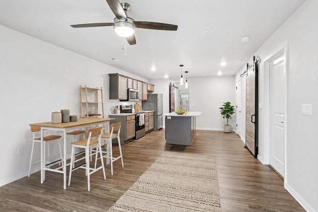 Open-plan kitchen with dark cabinets, wood floor, island, and sliding barn door leading to another room