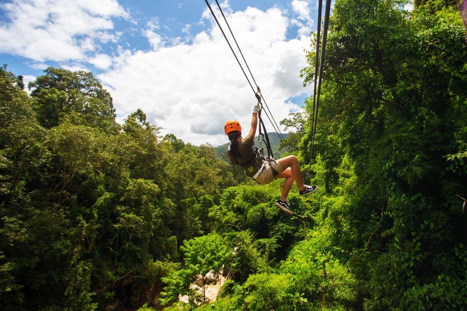 A person is flying through the air on a zip line in the jungle.