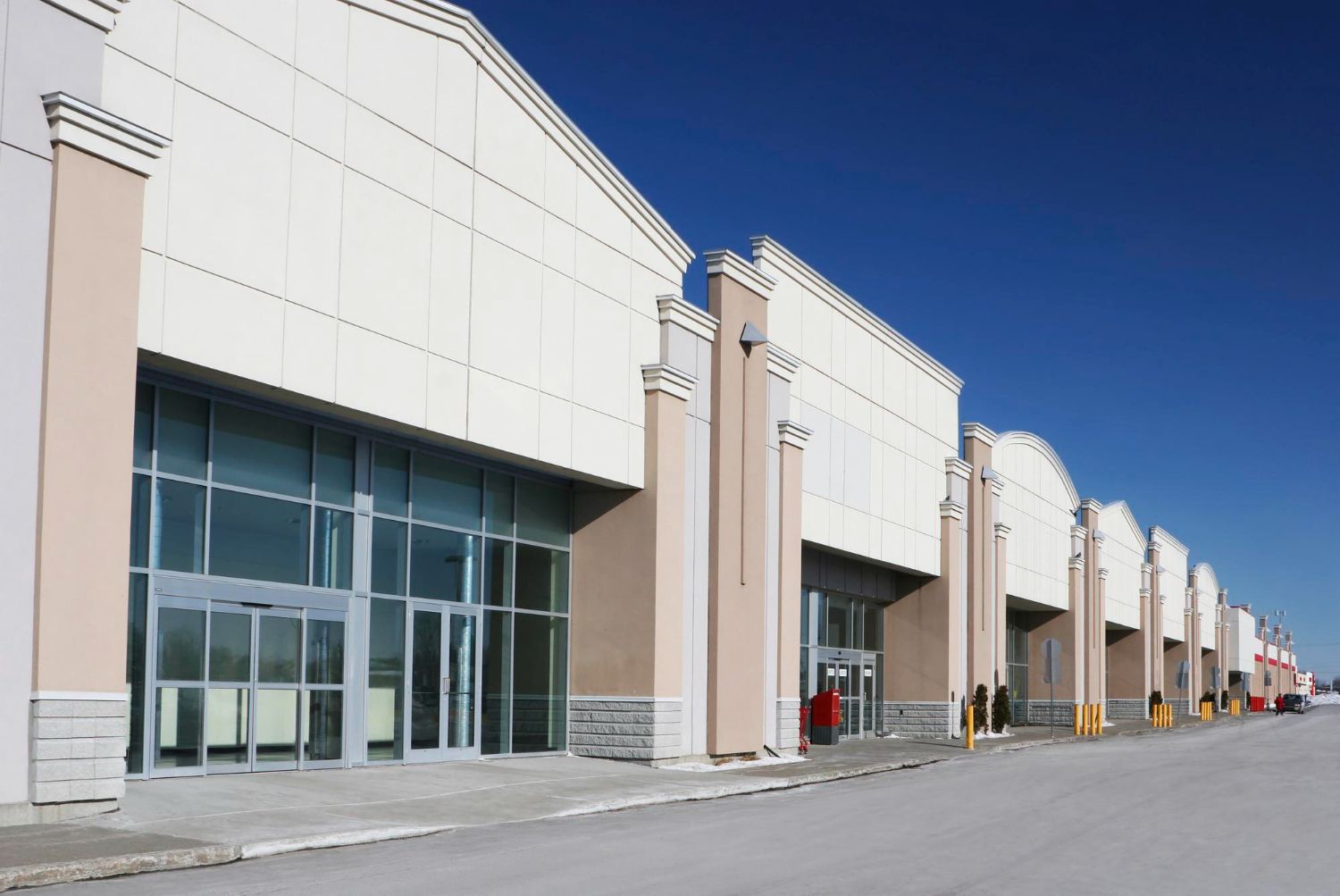 A large commercial building with storefronts and glass entrances under a clear blue sky.