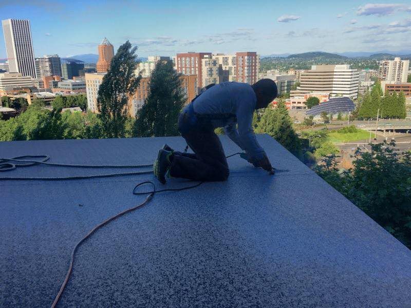 A man is kneeling on a roof with a city in the background.