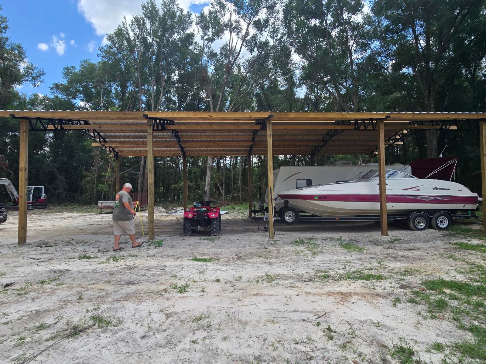 Wooden boat shelter with a person, an ATV, and a white-and-maroon speedboat on a trailer.