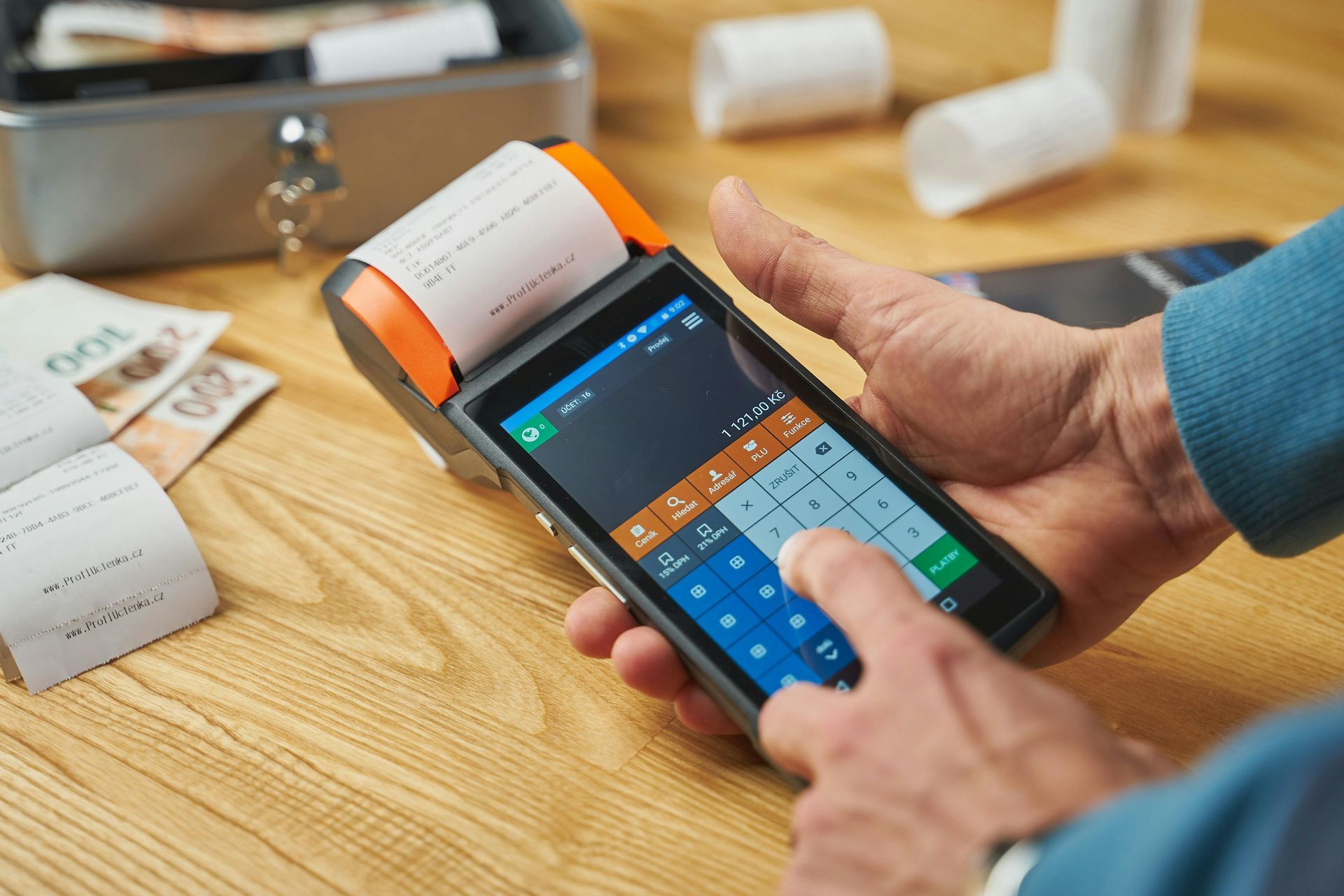 Person using a handheld card reader to enter a payment on a smartphone at a wooden table