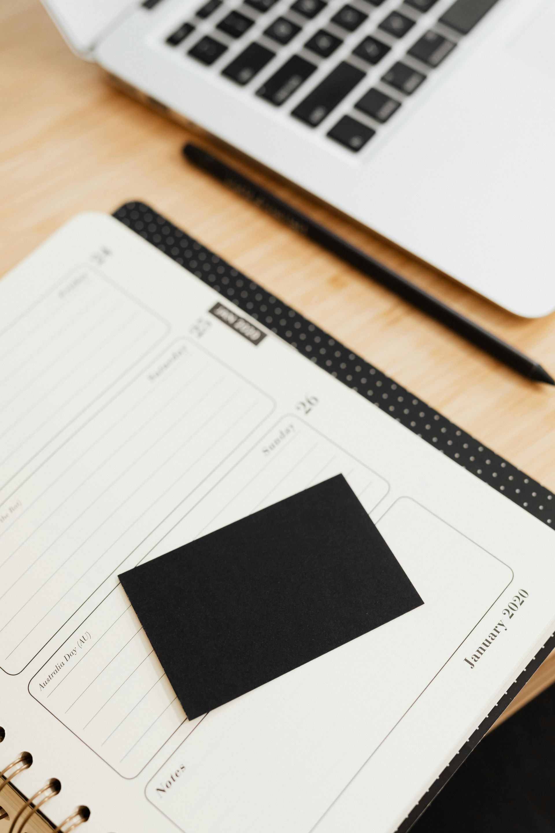 Open planner notebook with black cover beside a laptop on a wooden desk