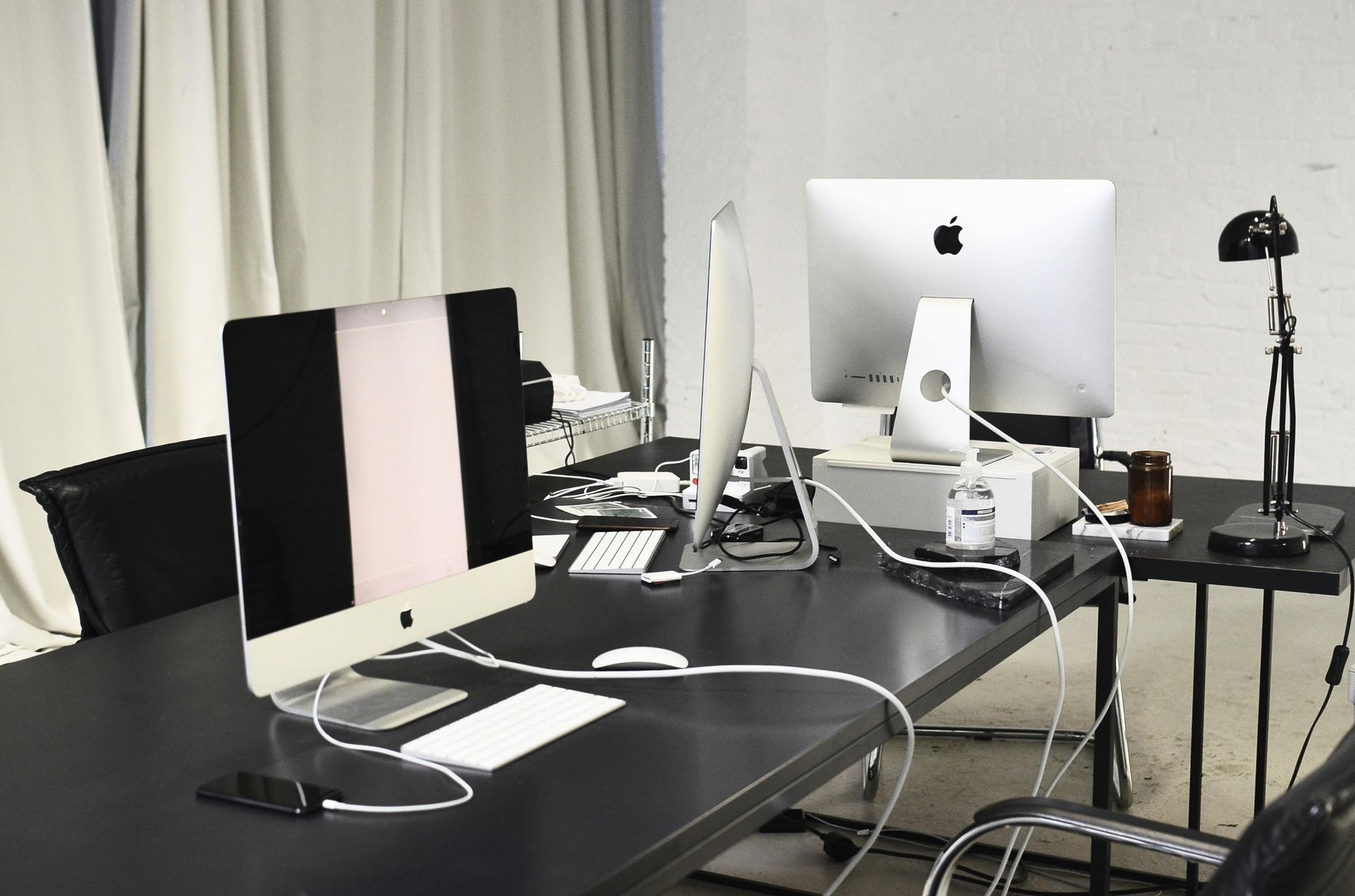 Cluttered desk with multiple Apple iMacs, cables, and a tripod in a studio-like room