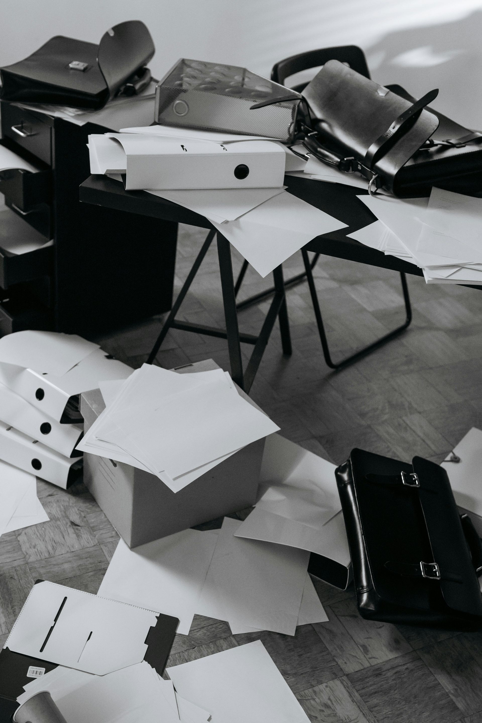 Scattered white papers and black chairs in a messy room with a desk and chair overturned
