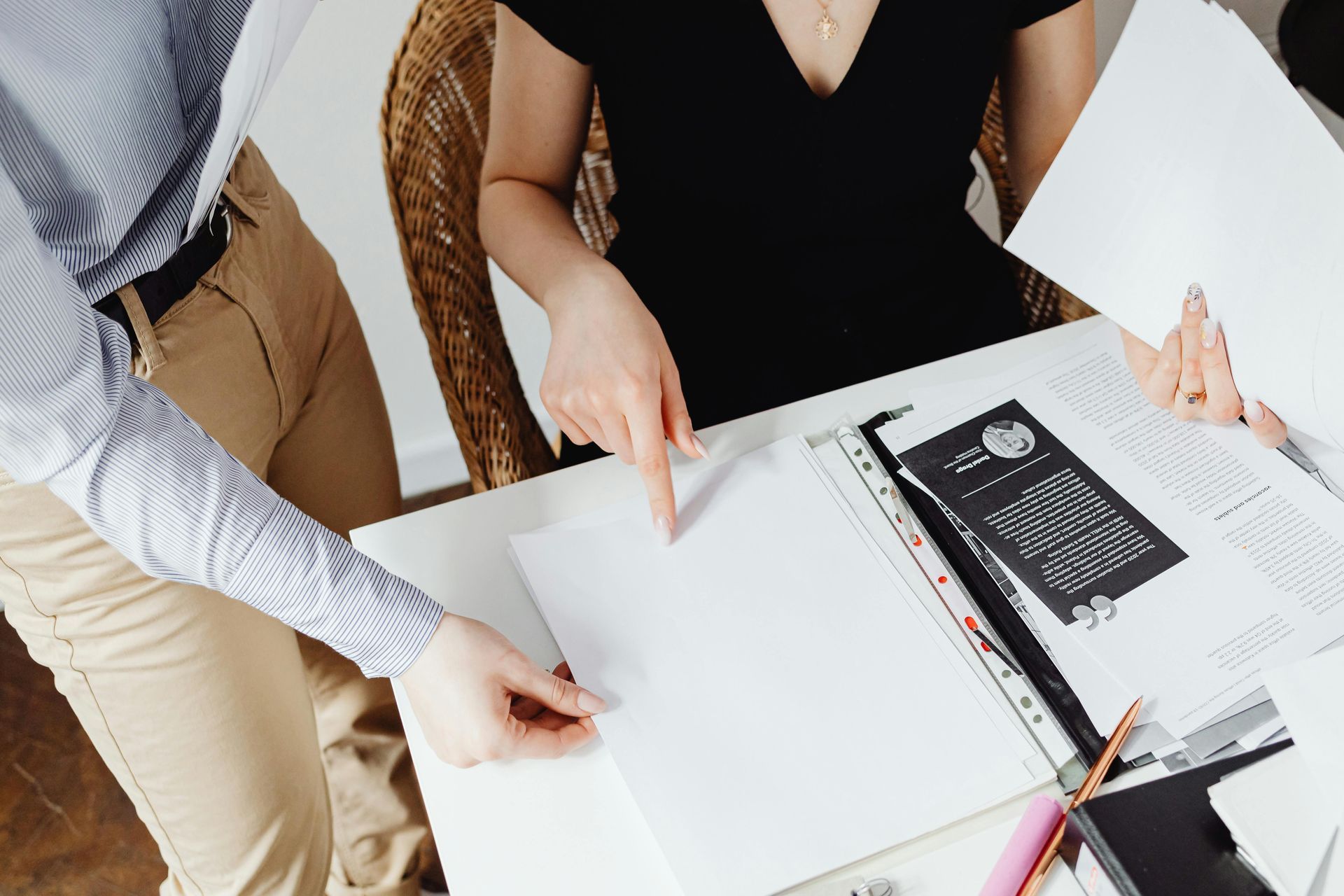 People collaborating at a desk with papers, notebooks, and a laptop in a bright office.