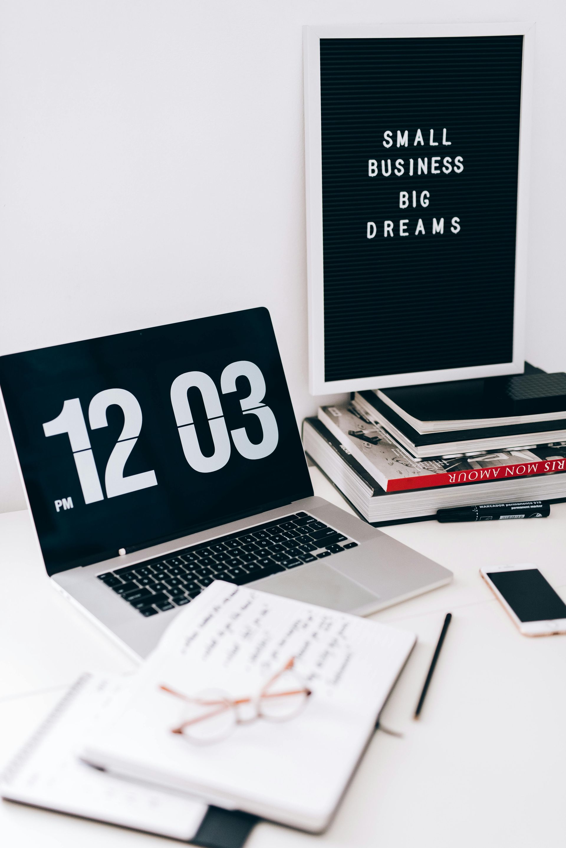Workspace with laptop, flip clock showing 12:03, and letter board reading “Small business big dreams”