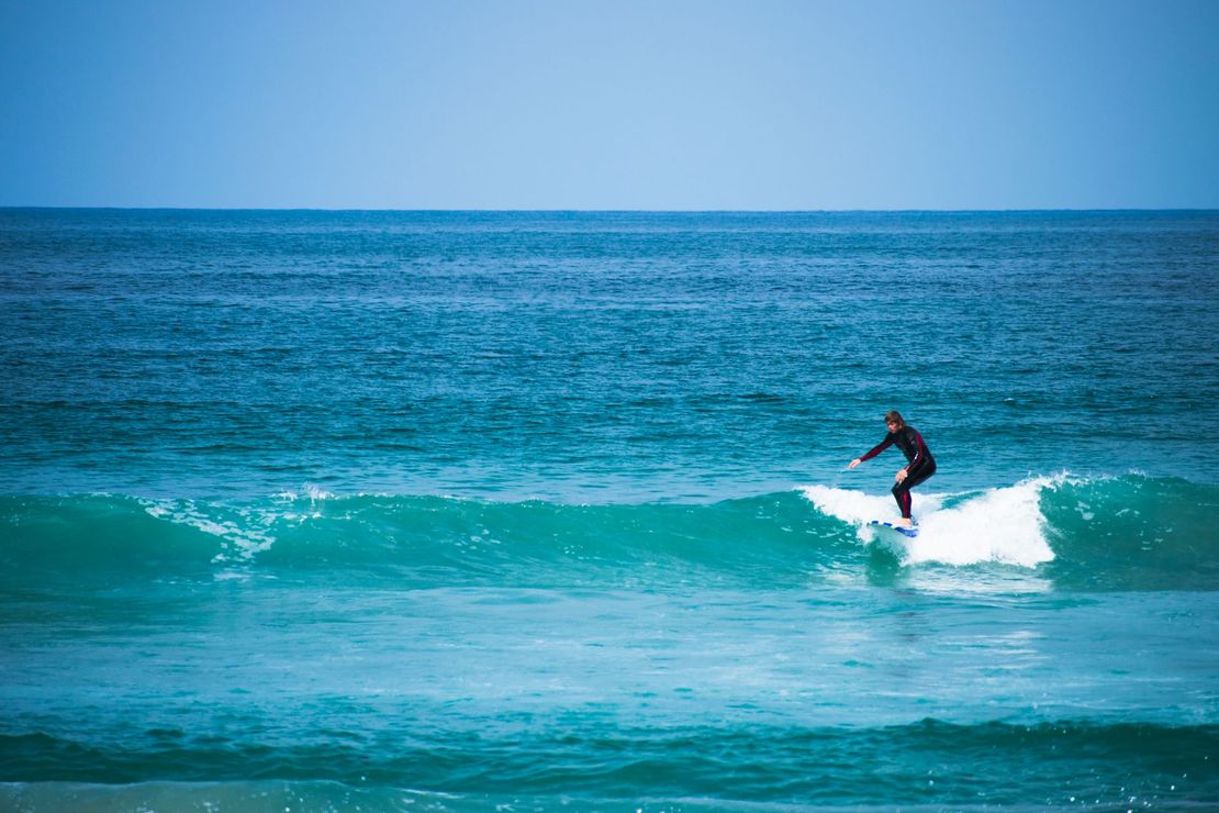Person surfing a wave in the ocean. Surfer is wearing a black wetsuit. Blue sky and ocean.