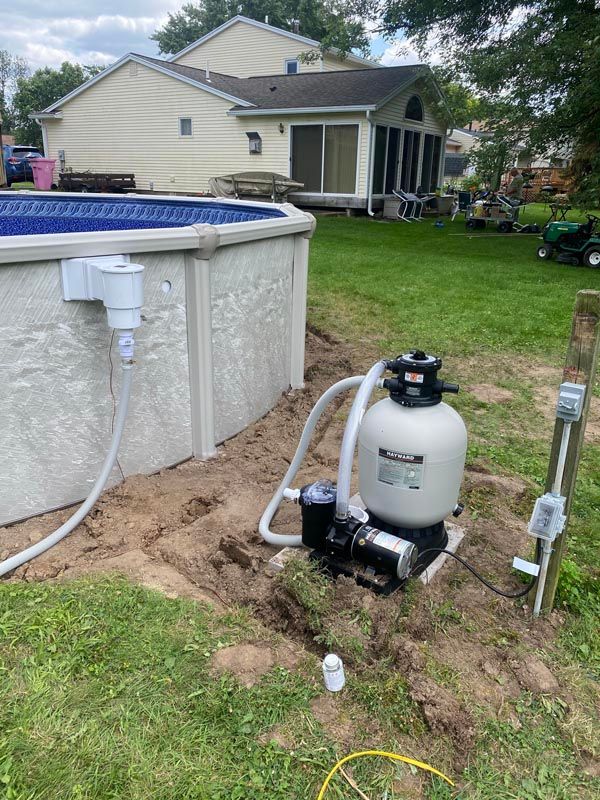 Backyard pool equipment with a white filter tank and pipes beside an above-ground pool and house