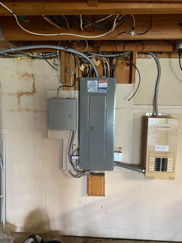 Electrical breaker panels and exposed wiring mounted on a basement wall.