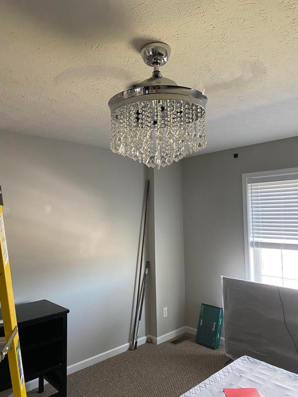 Bedroom corner with a crystal chandelier, gray walls, carpet, and a bed partially visible.