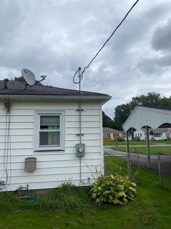 Side of a small white house with a satellite dish, power line, and cloudy sky over a grassy yard.