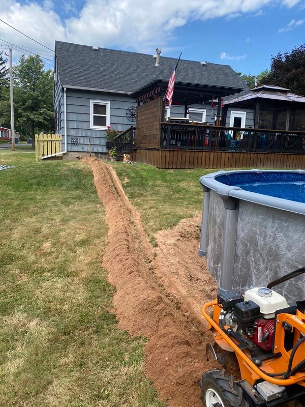 Backyard with a fresh dirt trench leading to a gray house, blue above-ground pool at right, and orange pump in foreground
