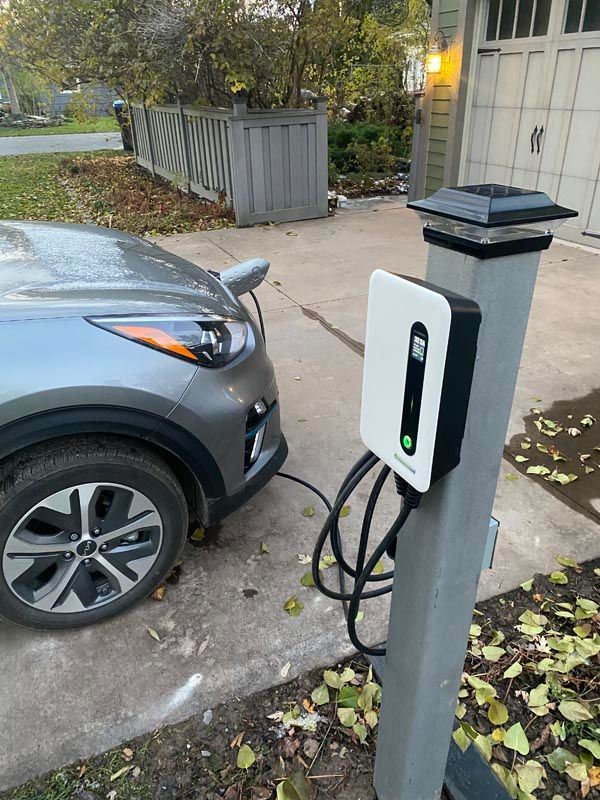 Electric car plugged into a white charging station on a driveway beside a house and garage.