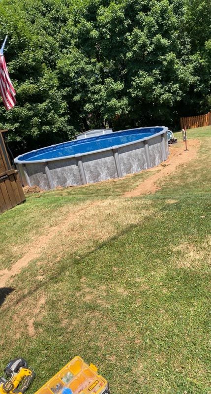 Above-ground pool in a backyard with grass, wooden fence, and an American flag on the left.