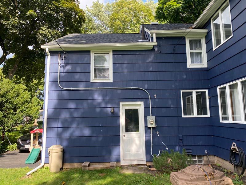 Blue house exterior with white trim, back door, and windows in a leafy yard