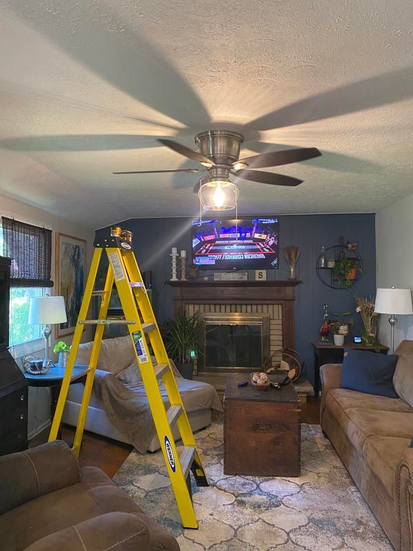 Living room with a yellow ladder under a ceiling fan and a TV above a fireplace