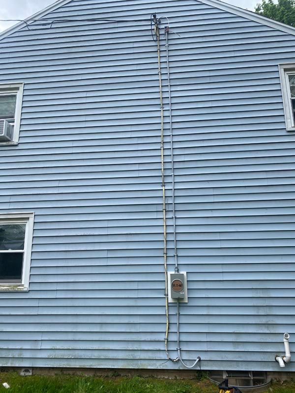 Blue house siding with vertical utility pipes and meter box on the exterior wall.