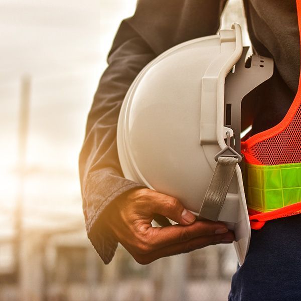 Worker holding a white hard hat beside a neon safety vest at a construction site