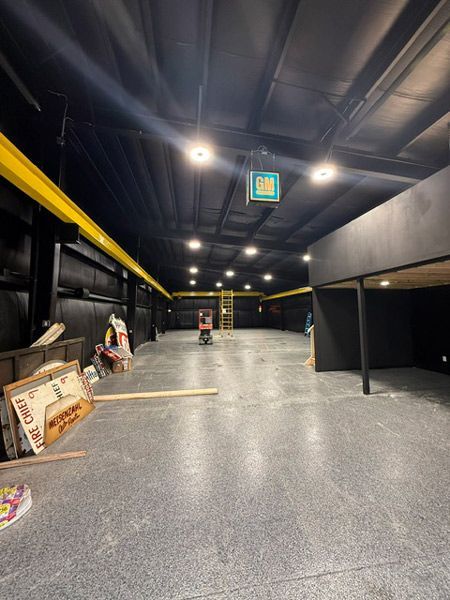 Empty indoor hall with black ceiling, gray floor, yellow beams, and a few signs and items along the sides