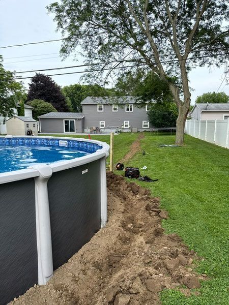 Backyard above-ground pool beside a freshly dug trench, with a grassy yard and house in the background