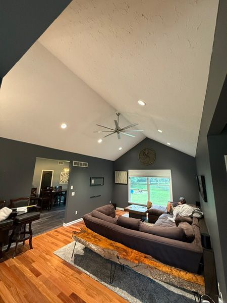 Spacious living room with vaulted ceiling, large sofa, ceiling fan, and a bright TV on the far wall