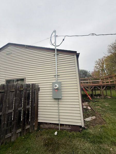 Back of beige house with electrical meter and overhead utility line in a grassy yard
