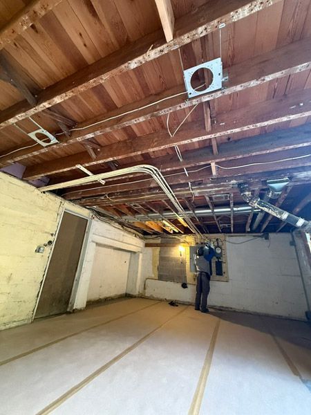 Underground basement under renovation with exposed ceiling beams, white walls, and construction materials on the floor